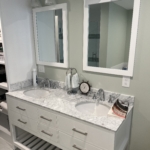 Double sink and vanity with a marble countertop and framed mirrors using overhead lighting and silver hardware